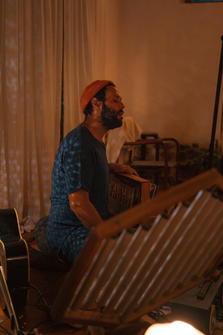 Man playing the shruti box and singing in a candlelit room during an intimate sound healing session.