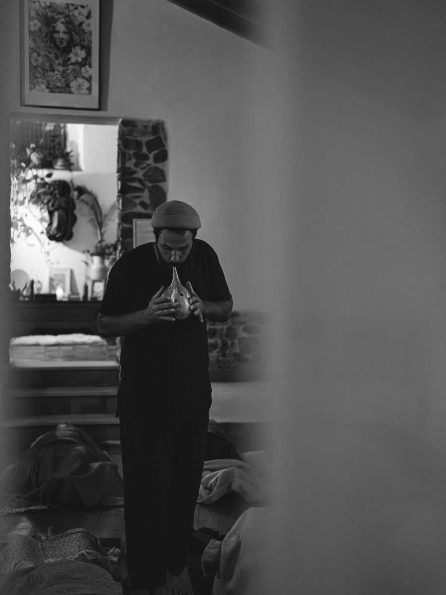 DSC00538-Verbeterd-NR-2 Black and white photo of Yoav playing a ceramic flute, standing amidst participants during a sound journey.