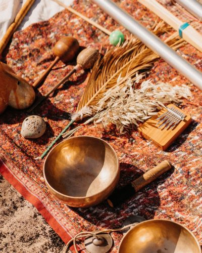 _PAN2824 Tibetan bowls, leaf shakers, and chimes resting on a warm-colored carpet in nature, ready for a sound healing session.